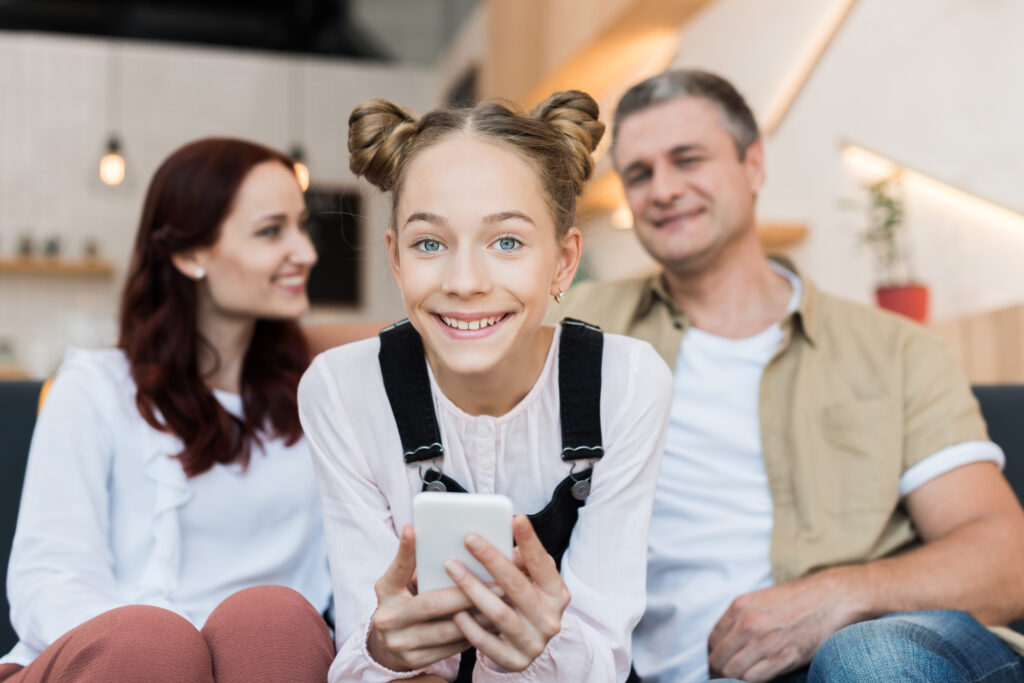 mature parents and teen girl with smartphone in cafe