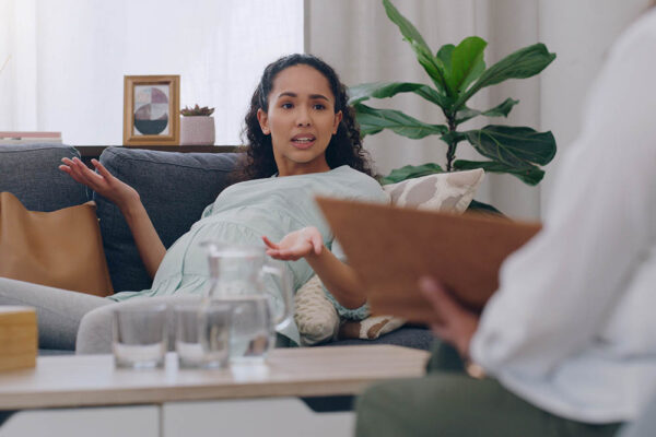 Mental health, pregnancy and woman on sofa in therapy or counseling session for depression, anxiety.
