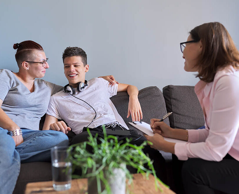 Mother with her teenage son at meeting with social worker, psychologist, discussing, mental health family, sitting on sofa in psychotherapist office