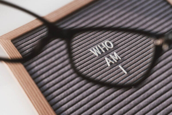 Top view on letterboard with words WHO AM I through eyeglasses. Flat lay concept of psychological self-regulation or gender identity. Social psychological issue. Closer look on psychological problems.